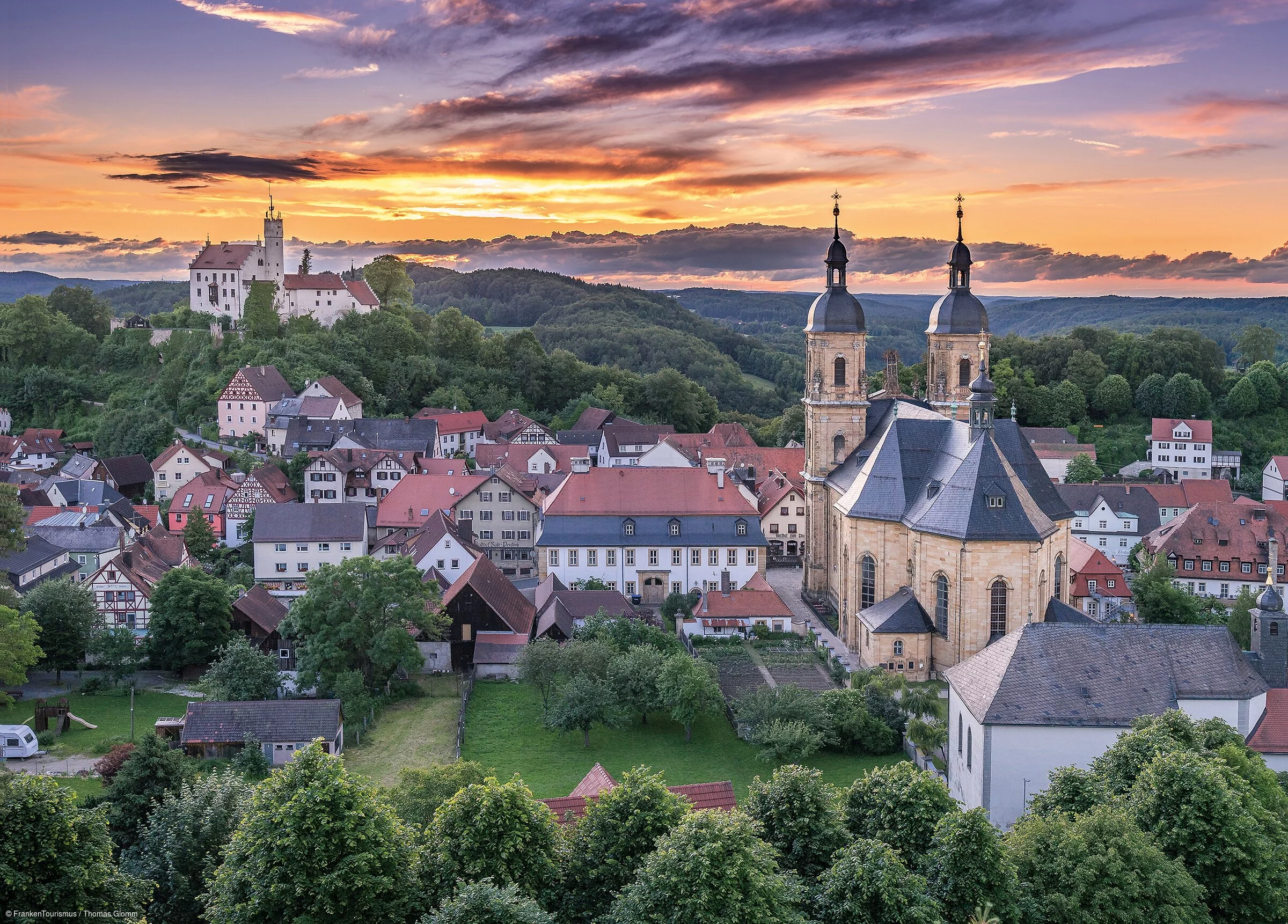 Blick über ein Dorf mit Klosterkirche im Vordergrund und Burg im Hintergrund