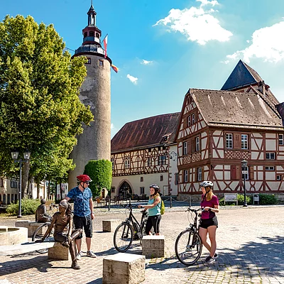 Vor einem historischen Gebäudekomplex mit Fachwerk steht eine Gruppe Radfahrer:innen