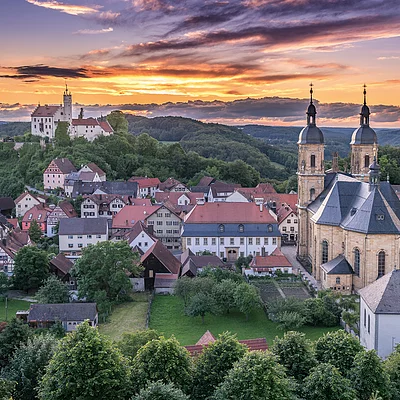 Blick über ein Dorf mit Klosterkirche im Vordergrund und Burg im Hintergrund