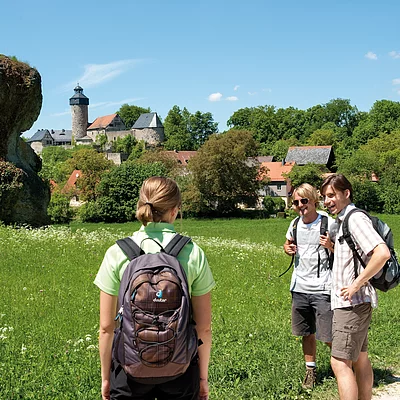 Eine Gruppe Wandernder vor einer grünen Wiese, im Hintergrund ist eine Burg zu erkennen.
