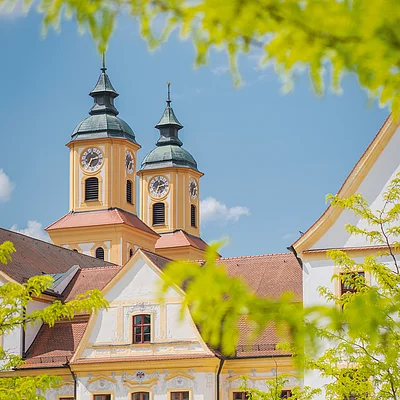 Zwei Personen fahren auf Fahrrädern vor einem historischen Gebäude mit zwei Kirchtürmen.