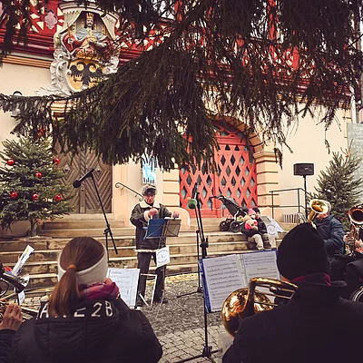 Eine Blaskapelle spielt vor einem historischen Gebäude mit weihnachtlicher Dekoration und Tannenbaum.