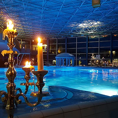 In der Spessart Therme bei Nacht mit Kerzenleuchtern im Vordergrund und beleuchtetem Pool.