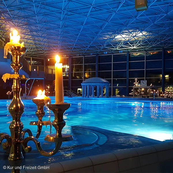 In der Spessart Therme bei Nacht mit Kerzenleuchtern im Vordergrund und beleuchtetem Pool.