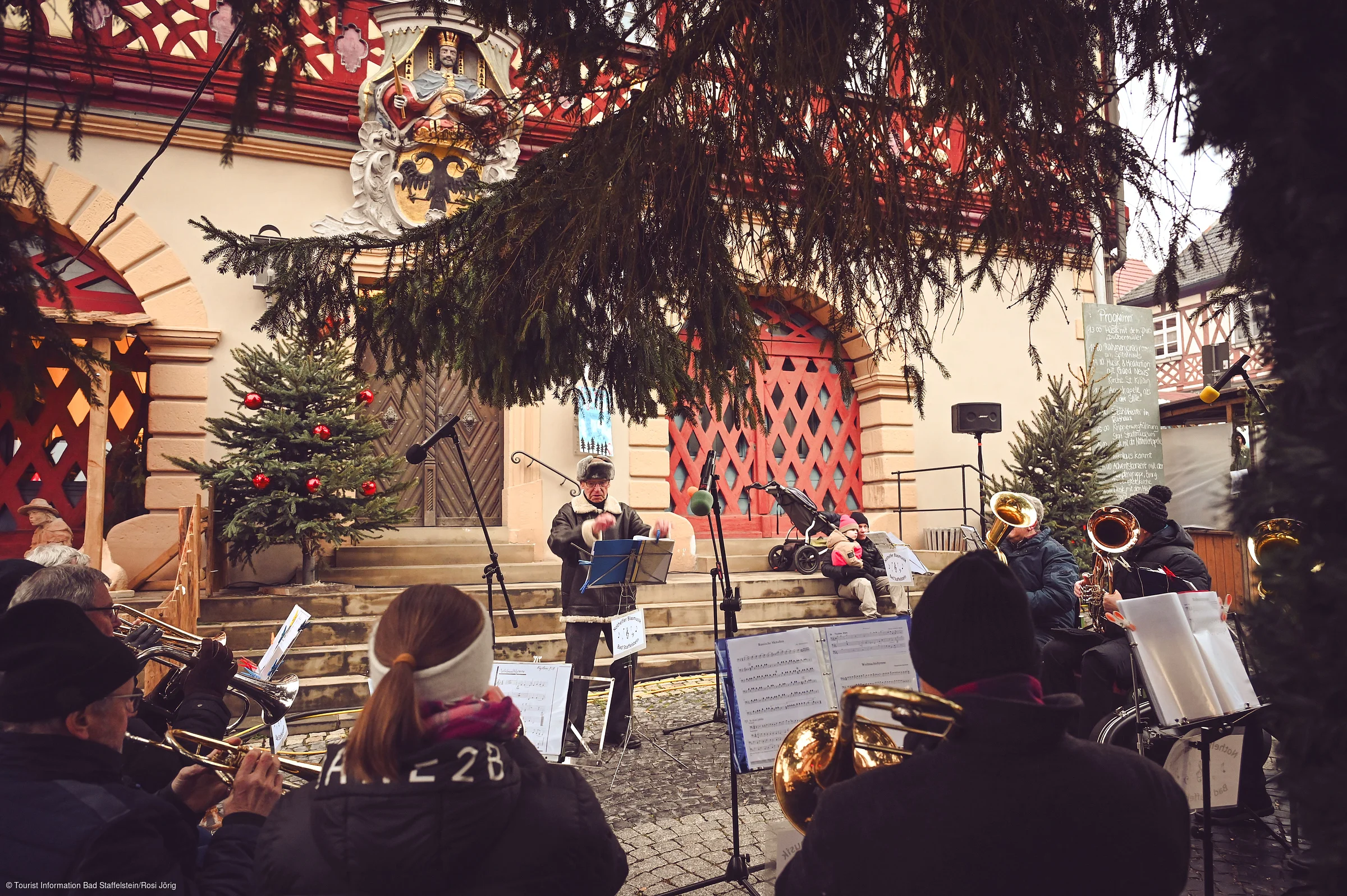 Eine Blaskapelle spielt vor einem historischen Gebäude mit weihnachtlicher Dekoration und Tannenbaum.