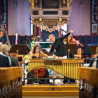 Musiker spielen Marimbaphon, Cello, Kontrabass und Violinen in einer Kirche vor Publikum.