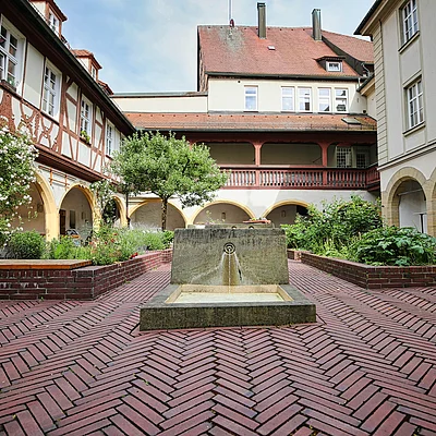 Innenhof mit Backsteinboden, Brunnen in der Mitte, Blumenbeeten und Fachwerkhäusern mit Arkaden.