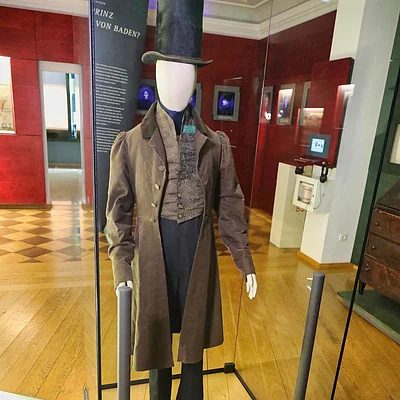 Historische Herrenmode mit Zylinder und Gehrock in einer Museumsvitrine auf Holzboden.