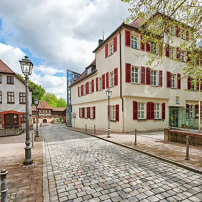 Pflasterstraße mit historischen Gebäuden und Laternen unter bewölktem Himmel in einer Altstadt.