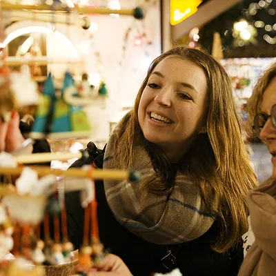 Zwei Frauen mit Schals betrachten und wählen Weihnachtsdekoration an einem Marktstand bei Nacht.
