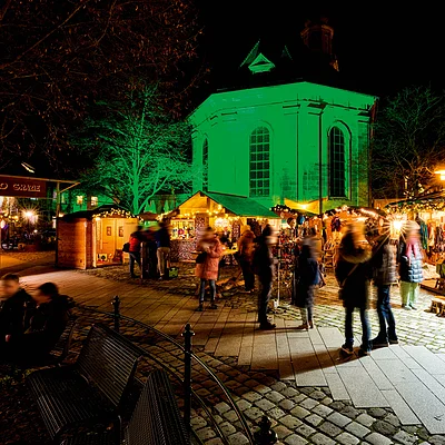 Weihnachtsmarkt mit beleuchteten Ständen und Menschen vor einer Kirche bei Nacht