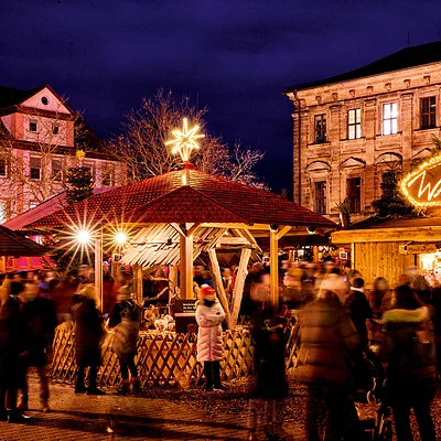 Weihnachtsmarkt bei Nacht mit beleuchteten Ständen und Menschen in Winterkleidung vor historischen Gebäuden