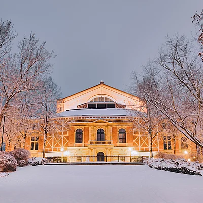 Beleuchtetes historisches Gebäude im Schnee, umgeben von schneebedeckten Bäumen bei Abenddämmerung.