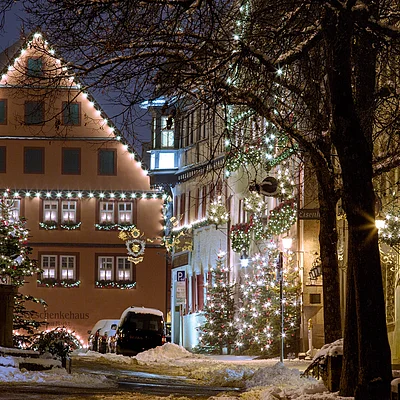 Weihnachtlich beleuchtete Fachwerkhäuser und geschmückte Tannenbäume an einem verschneiten Abend in einer Altstadt