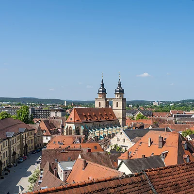 Stadtansicht mit roten Dächern und einer Kirche mit zwei Türmen unter blauem Himmel.