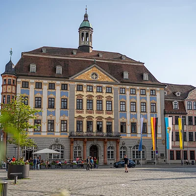 Historisches Rathaus mit Turm und Fahnen auf einem gepflasterten Platz bei Tageslicht