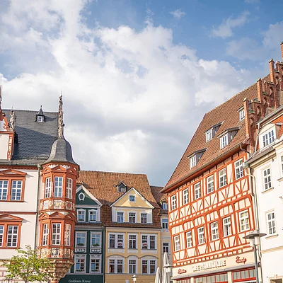 Historische Fachwerkhäuser und Außengastronomie an gepflastertem Platz unter bewölktem Himmel.