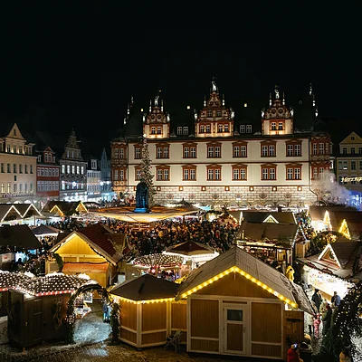 Weihnachtsmarkt mit beleuchteten Holzständen und vielen Besuchern vor historischem Rathaus bei Nacht.