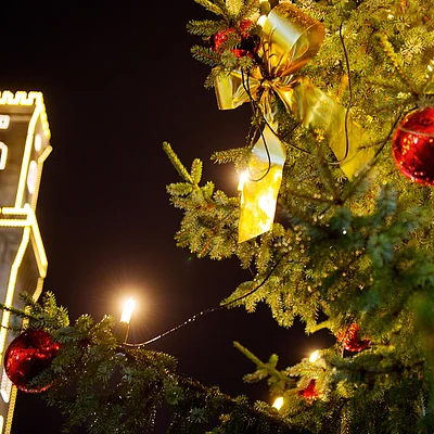 Weihnachtsbaum mit roten Kugeln und Lichtern, beleuchteter Rathausturm im Hintergrund bei Nacht
