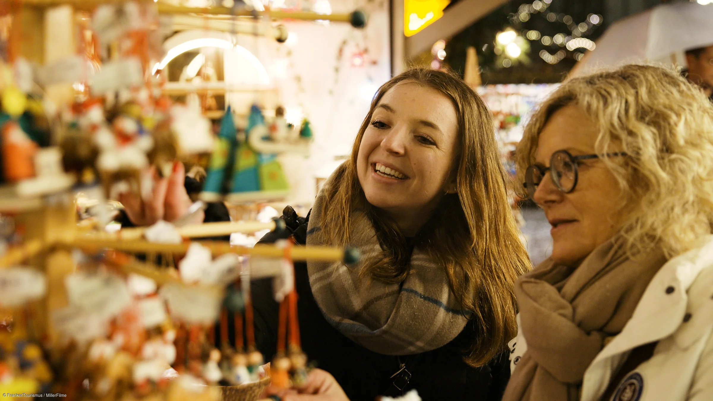 Zwei Frauen mit Schals betrachten und wählen Weihnachtsdekoration an einem Marktstand bei Nacht.