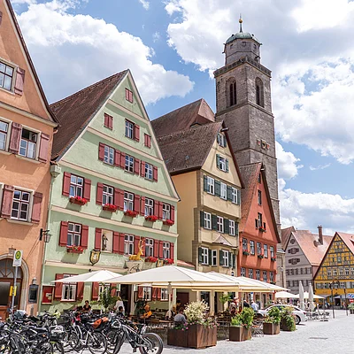 Altstadt mit Fachwerkhäusern, Außengastronomie, Fahrrädern und Kirchturm unter blauem Himmel mit Wolken