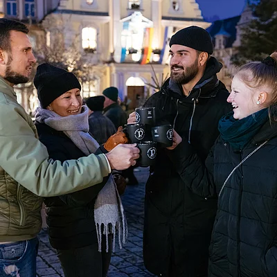 Vier Personen stoßen mit schwarzen Bechern bei einem abendlichen Treffen im Freien an.