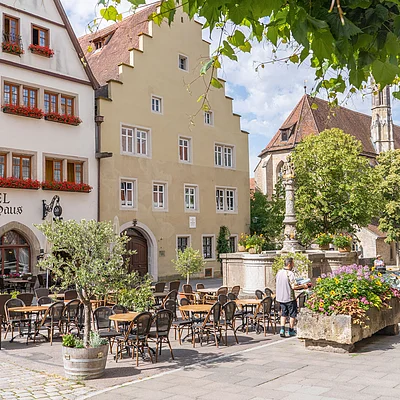 Außenbereich eines Hotels mit Tischen, Stühlen, Blumen und historischen Gebäuden im Hintergrund.