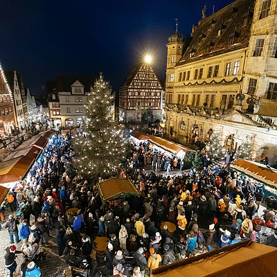 Weihnachtsmarkt mit beleuchtetem Baum und vielen Besuchern vor historischen Fachwerkhäusern bei Nacht