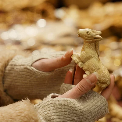 Hände mit grauen Handschuhen halten eine kleine geschnitzte Holzfigur eines Esels, unscharfer Hintergrund.