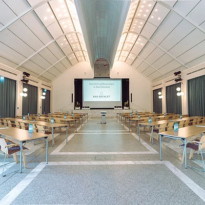 Konferenzraum mit Tischen, Stühlen, Wasserflaschen und Leinwand mit Begrüßungstext in Bad Bocklet.