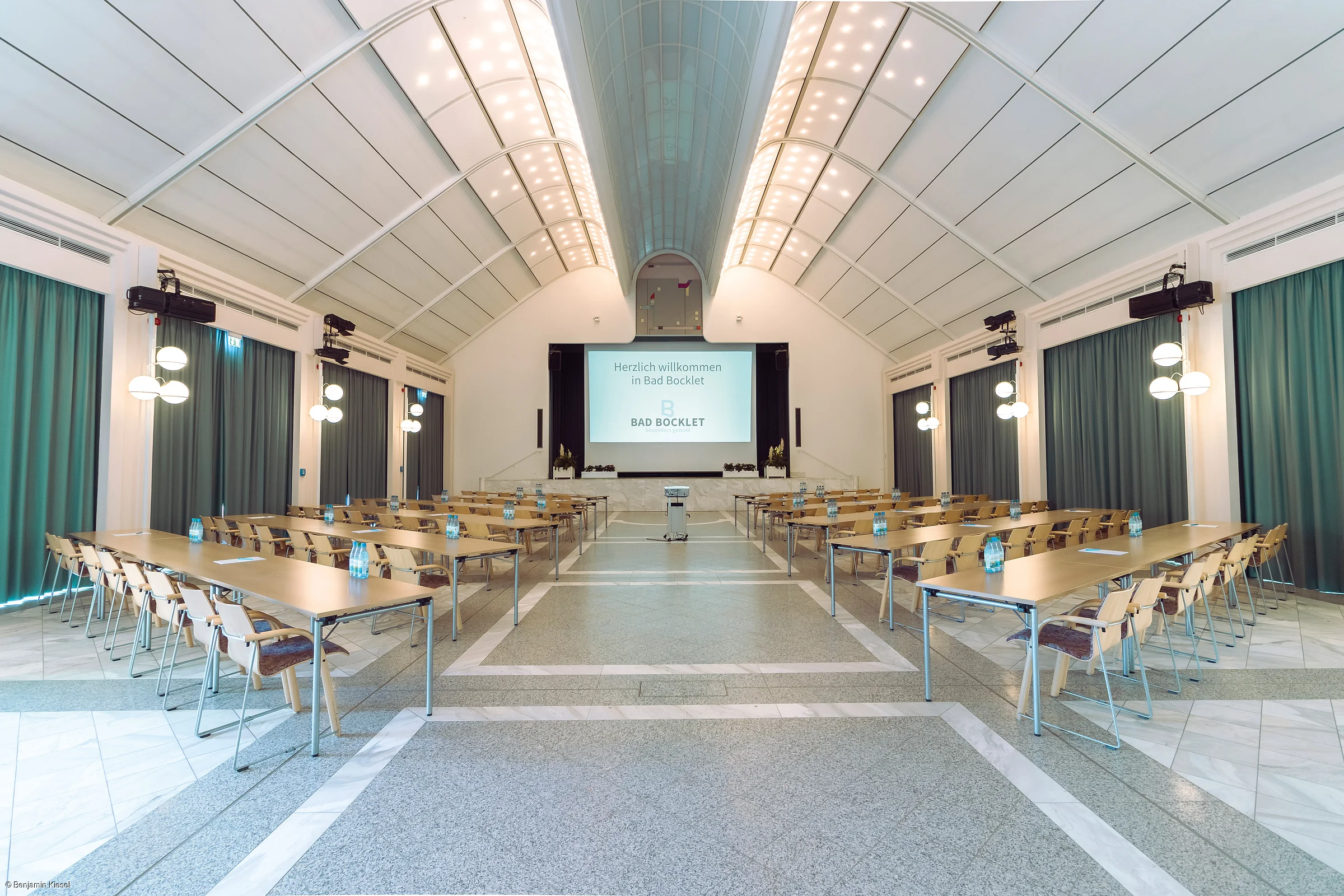 Konferenzraum mit Tischen, Stühlen, Wasserflaschen und Leinwand mit Begrüßungstext in Bad Bocklet.