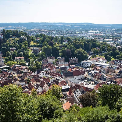 Blick auf eine Stadt mit vielen Häusern, Bäumen und Hügeln im Hintergrund bei klarem Himmel.