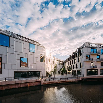 Moderne Gebäude am Wasser mit vielen Fenstern und bewölktem Himmel bei Sonnenuntergang