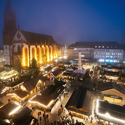 Weihnachtsmarkt mit beleuchteten Ständen und Kirche im Hintergrund bei Abenddämmerung und Nebel