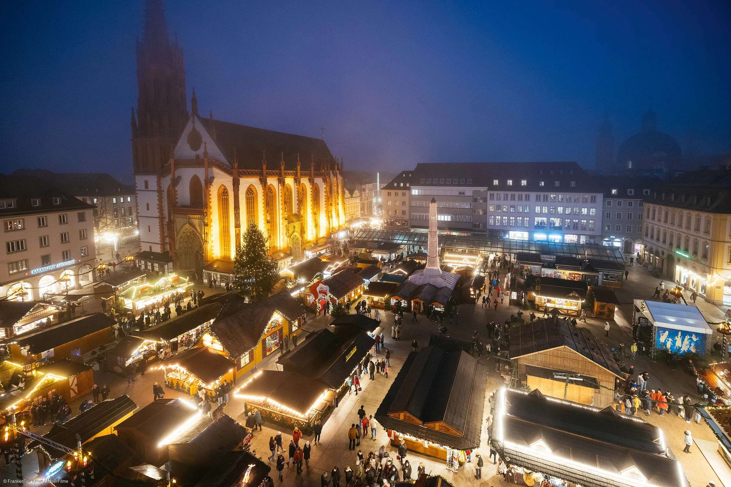 Weihnachtsmarkt mit beleuchteten Ständen und Kirche im Hintergrund bei Abenddämmerung und Nebel
