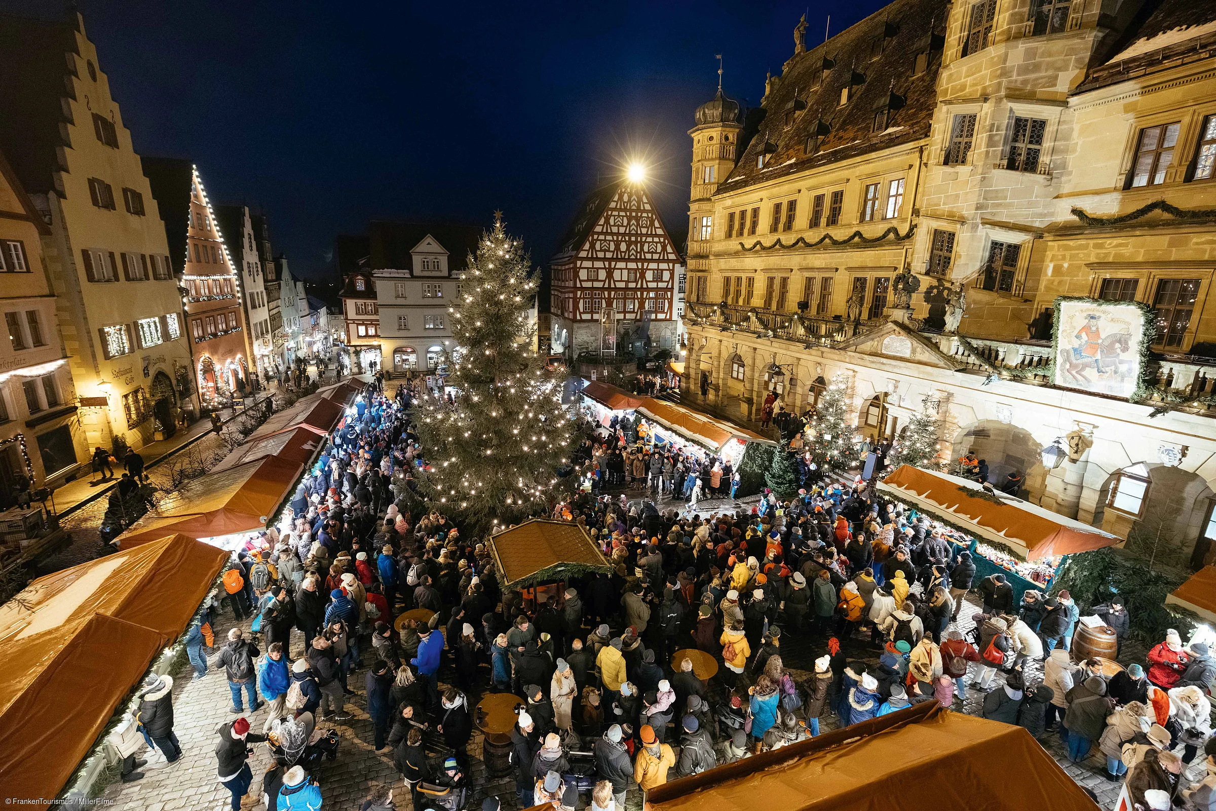 Weihnachtsmarkt mit beleuchtetem Baum und vielen Besuchern vor historischen Fachwerkhäusern bei Nacht