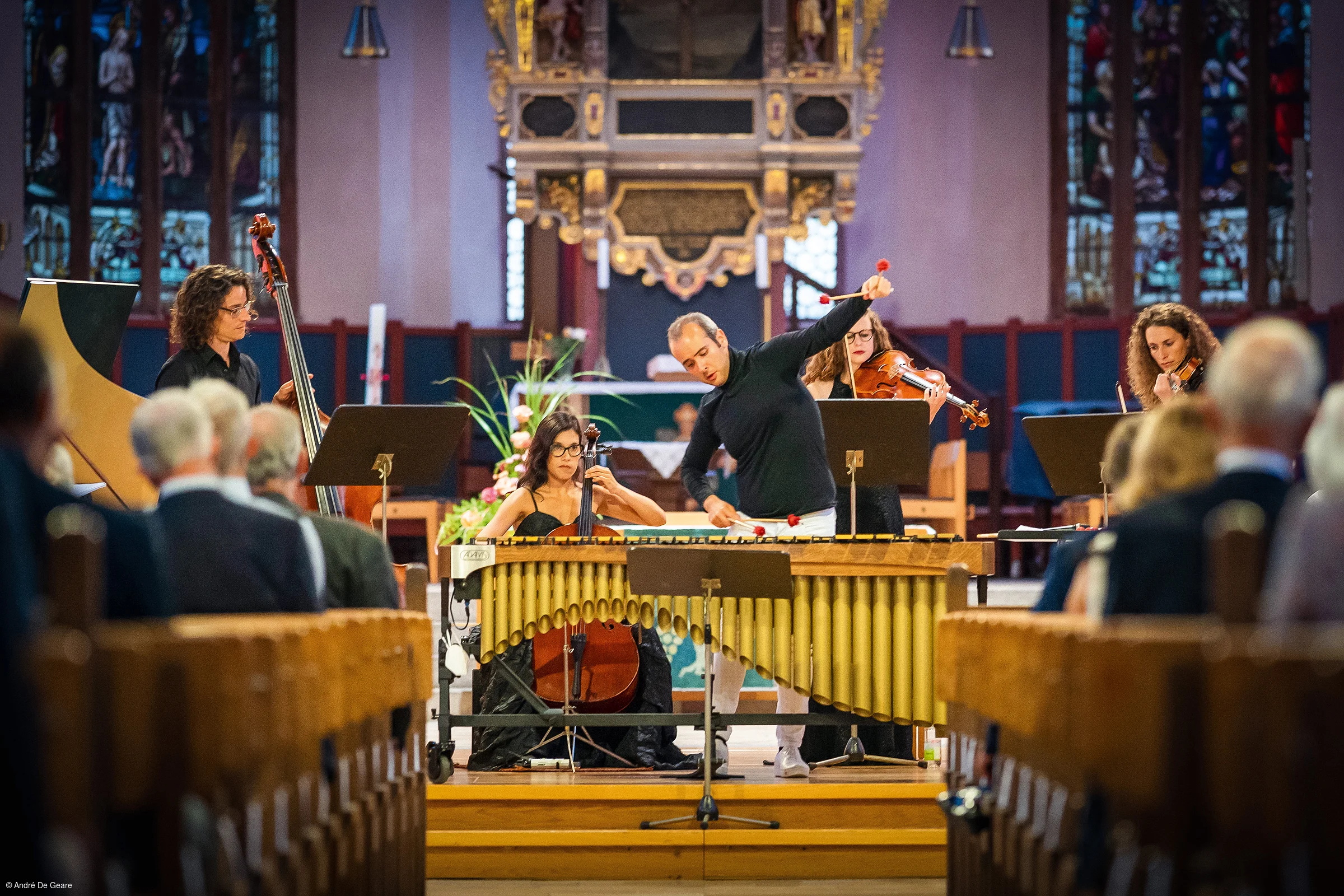 Musiker spielen Marimbaphon, Cello, Kontrabass und Violinen in einer Kirche vor Publikum.