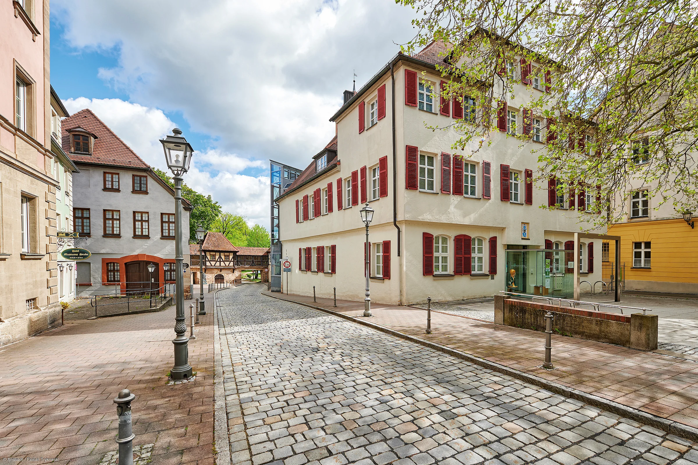 Pflasterstraße mit historischen Gebäuden und Laternen unter bewölktem Himmel in einer Altstadt.