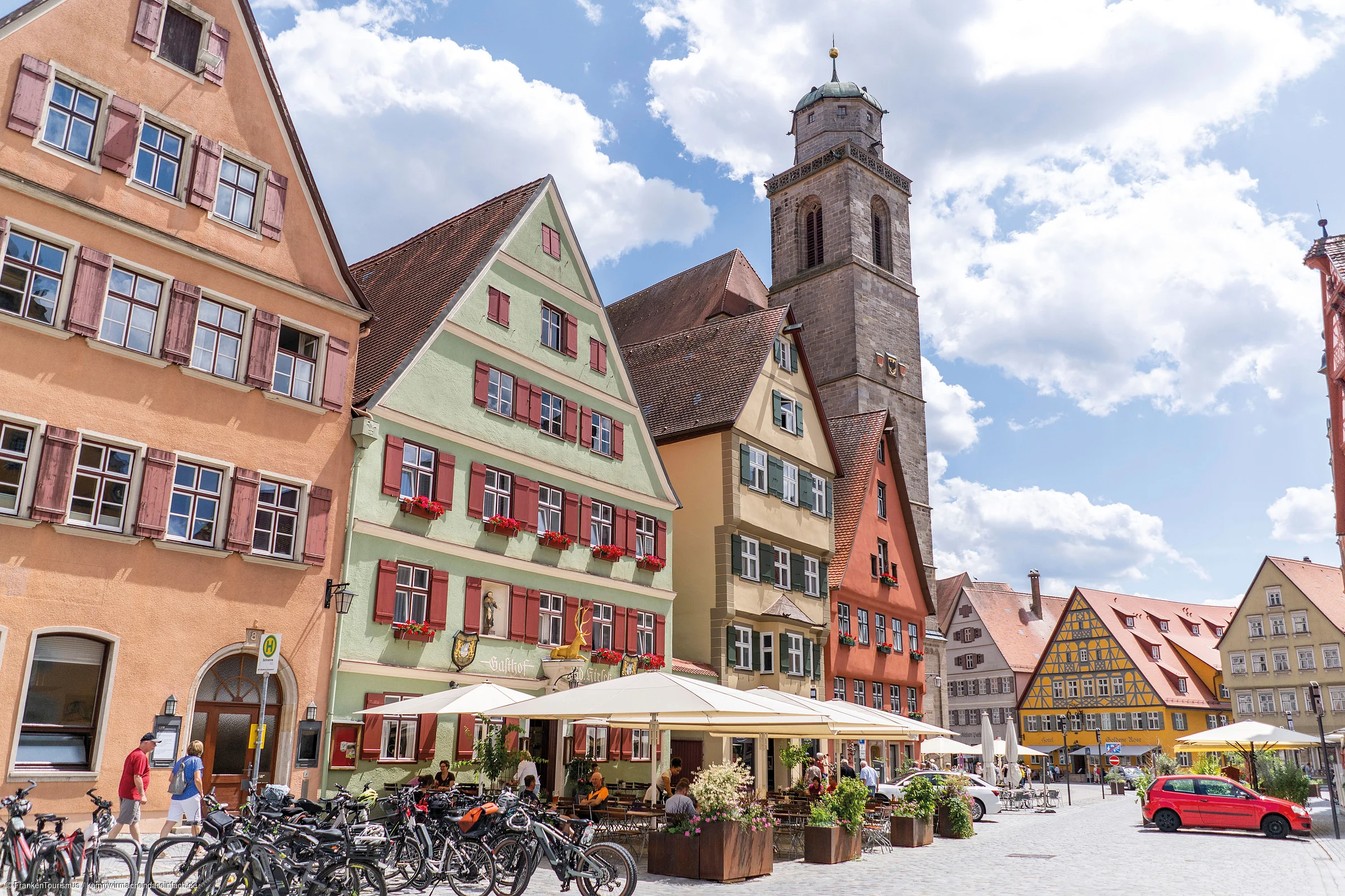 Altstadt mit Fachwerkhäusern, Außengastronomie, Fahrrädern und Kirchturm unter blauem Himmel mit Wolken