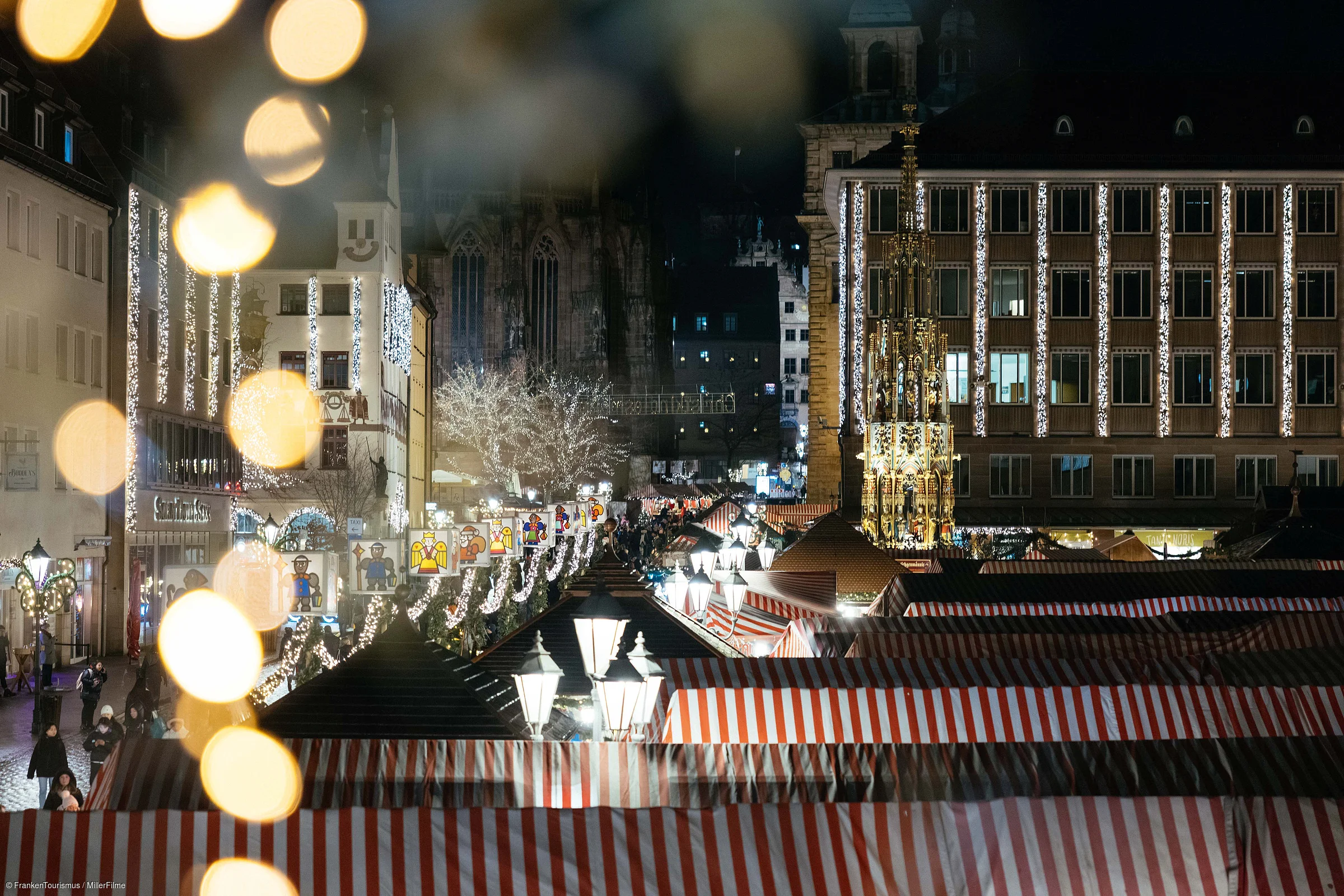Weihnachtsmarkt mit rot-weiß gestreiften Ständen und beleuchteten Gebäuden bei Nacht in einer Stadt.