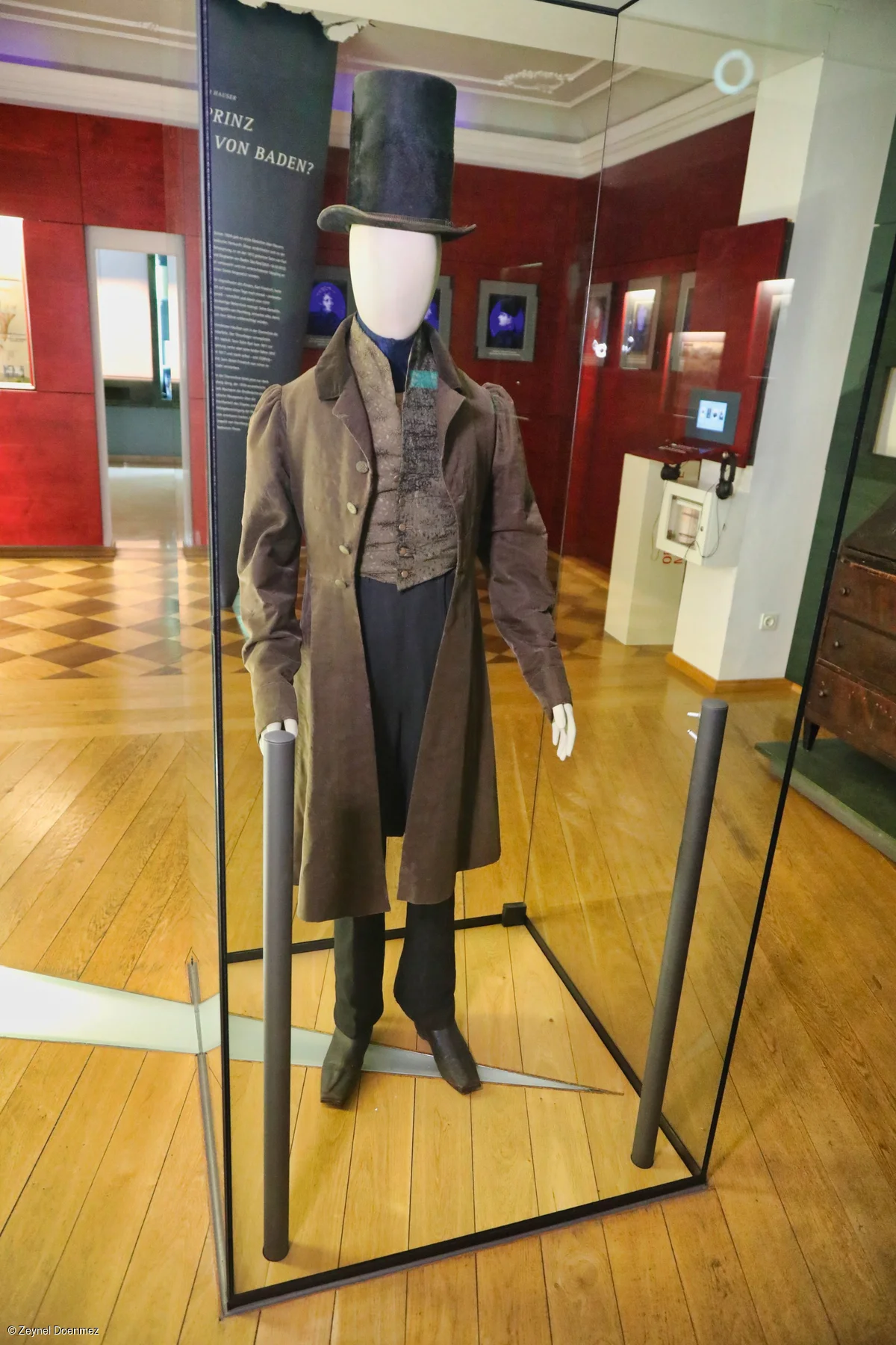 Historische Herrenmode mit Zylinder und Gehrock in einer Museumsvitrine auf Holzboden.