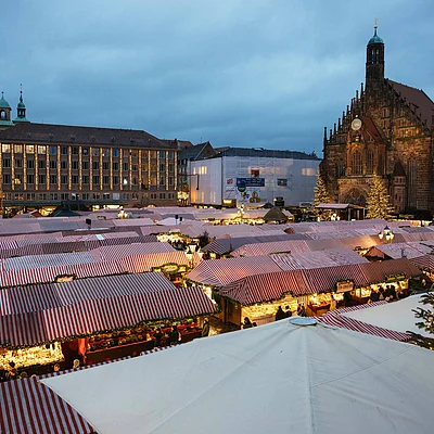 Weihnachtsmarkt mit beleuchteten Ständen und historischen Gebäuden bei Abenddämmerung unter bewölktem Himmel