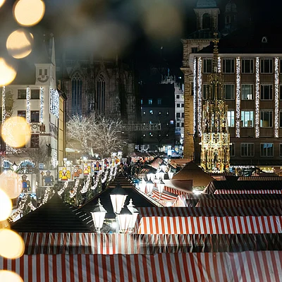 Weihnachtsmarkt mit rot-weiß gestreiften Ständen und beleuchteten Gebäuden bei Nacht in einer Stadt.