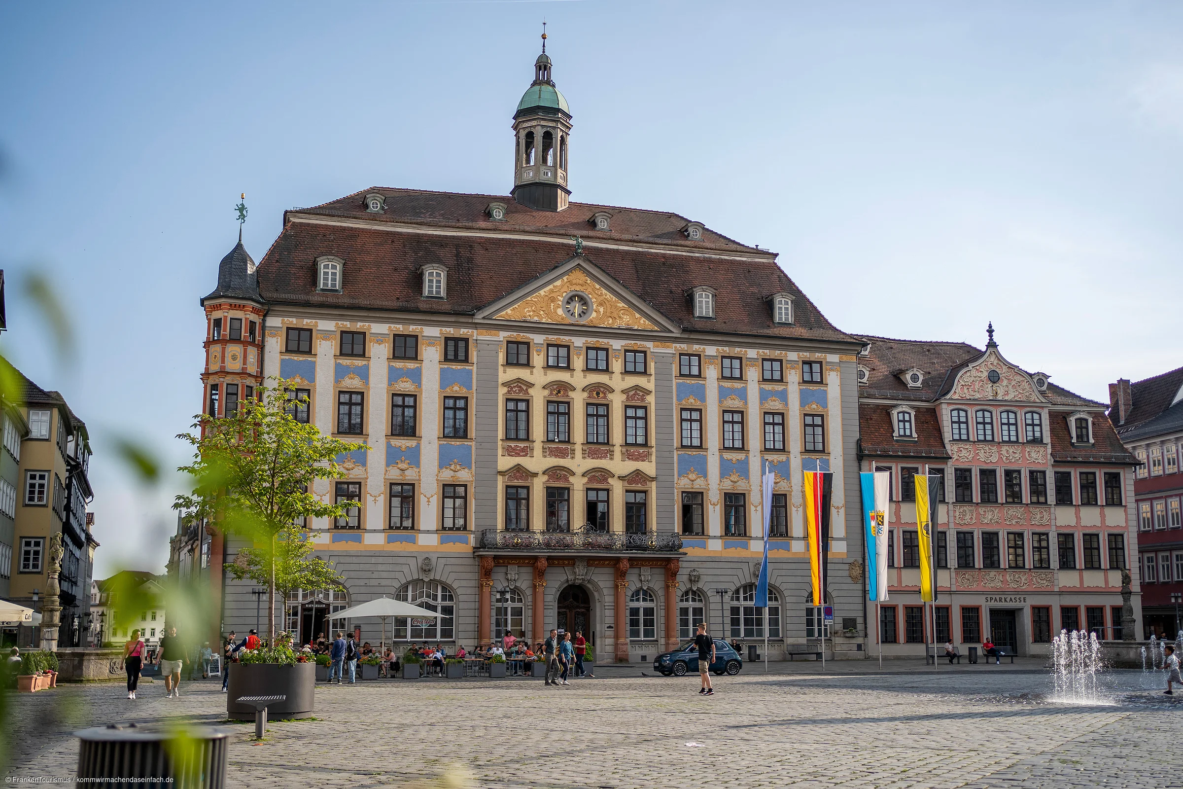 Historisches Rathaus mit Turm und Fahnen auf einem gepflasterten Platz bei Tageslicht