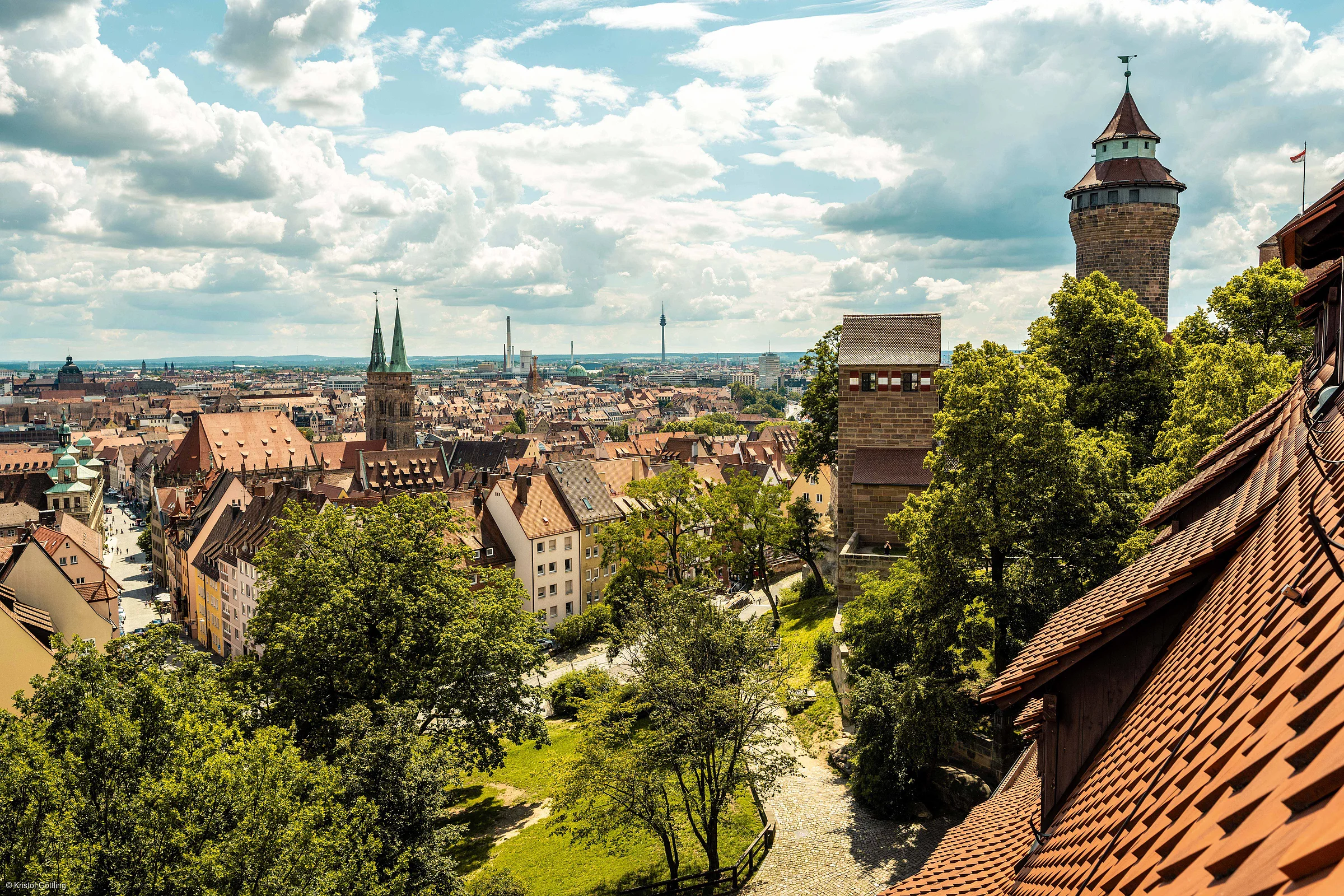 Blick über eine Stadt mit Fachwerkhäusern, zwei Kirchtürmen und einem historischen Turm bei bewölktem Himmel.