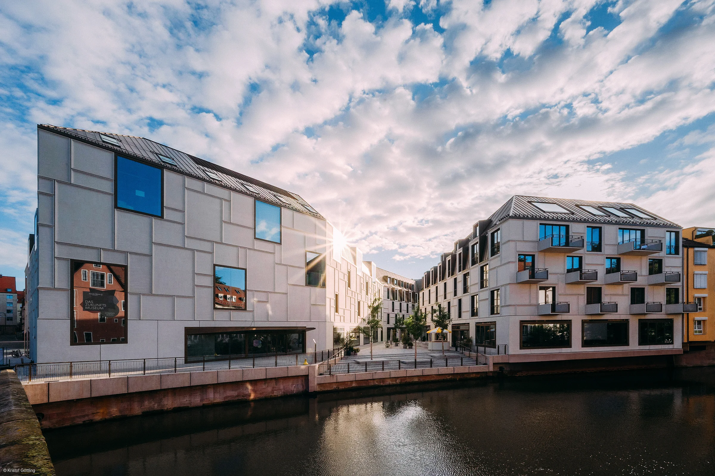 Moderne Gebäude am Wasser mit vielen Fenstern und bewölktem Himmel bei Sonnenuntergang