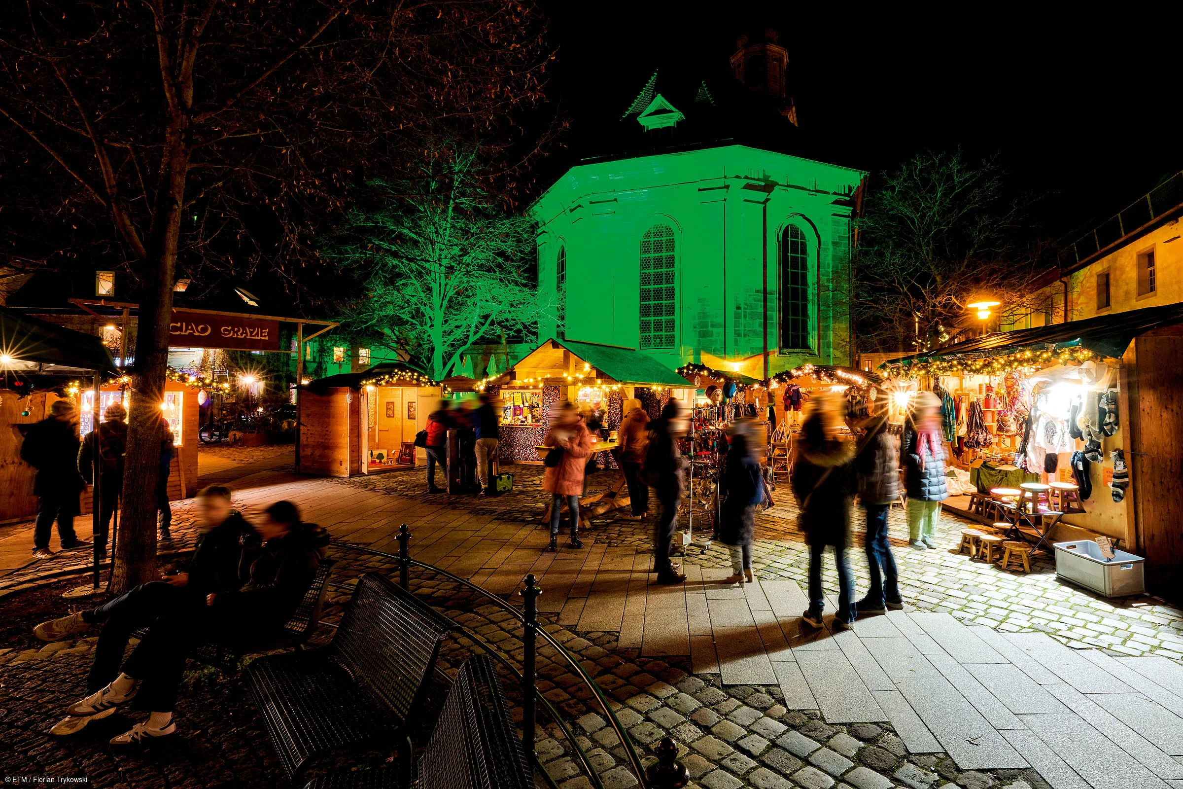 Weihnachtsmarkt mit beleuchteten Ständen und Menschen vor einer Kirche bei Nacht