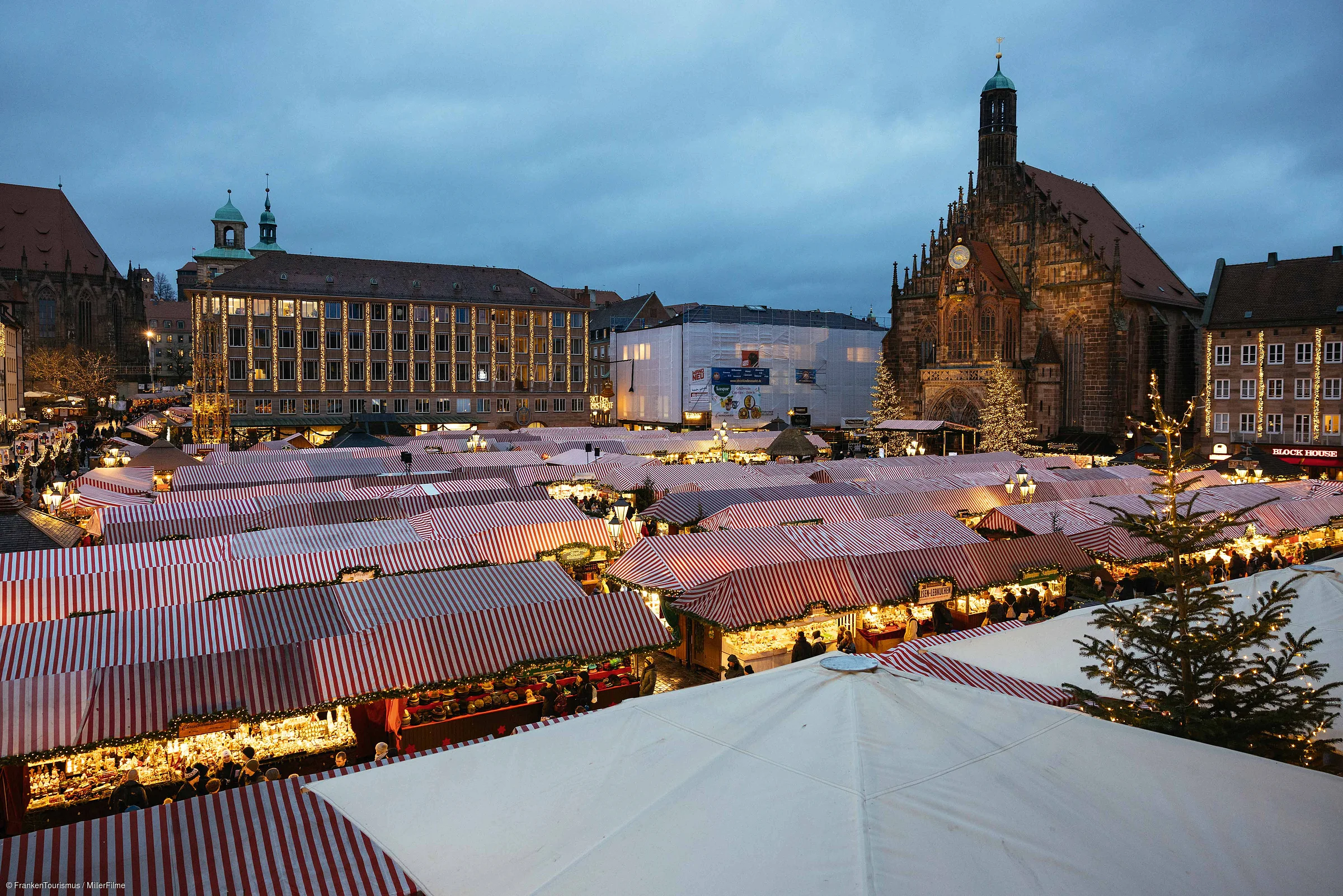 Weihnachtsmarkt mit beleuchteten Ständen und historischen Gebäuden bei Abenddämmerung unter bewölktem Himmel