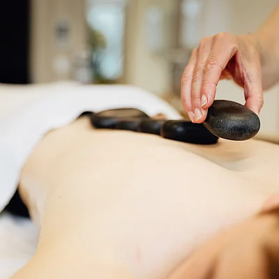 Hand legt schwarzen Hot-Stone auf nackten Rücken einer liegenden Person bei Massage.