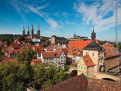 Blick über die Altstadt (Bamberg, Steigerwald) Eine Stadtansicht mit historischen Gebäuden, Kirchtürmen und Brücken bei blauem Himmel